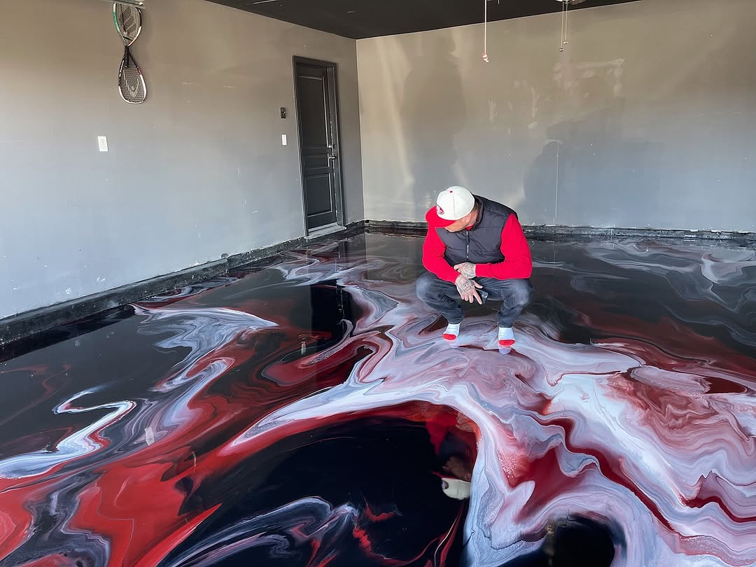 Johnny Mendoza of Gold Coast Resin crouched on a red and black metallic epoxy floor examining his work in Hollister, CA