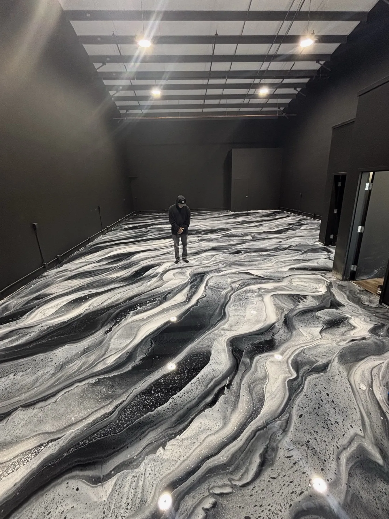 Black and silver metallic epoxy floor pouring across a dark showroom, the swirl pattern running the full length of the room