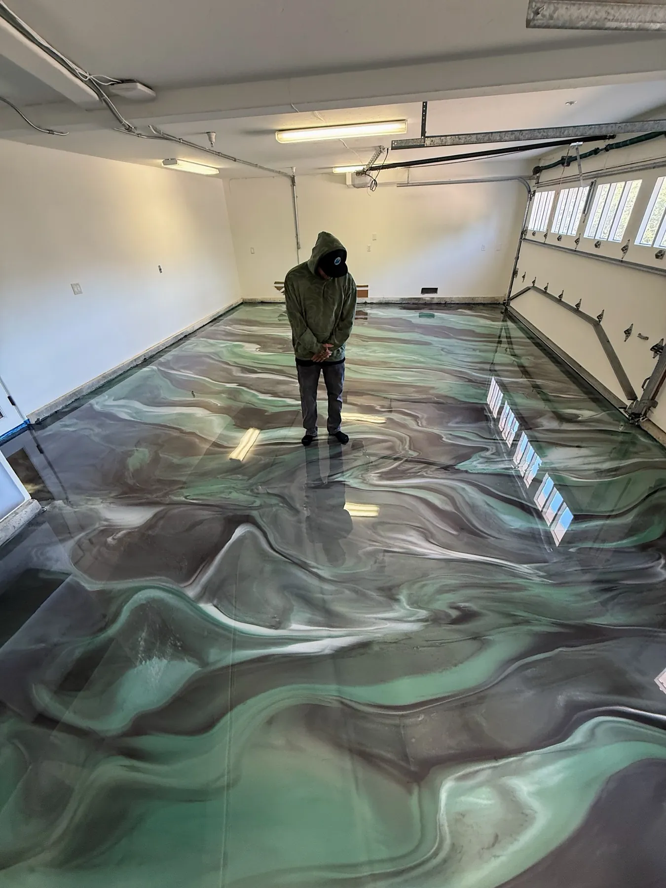 Sea green and charcoal metallic epoxy garage floor reflecting the shop windows in its gloss coat