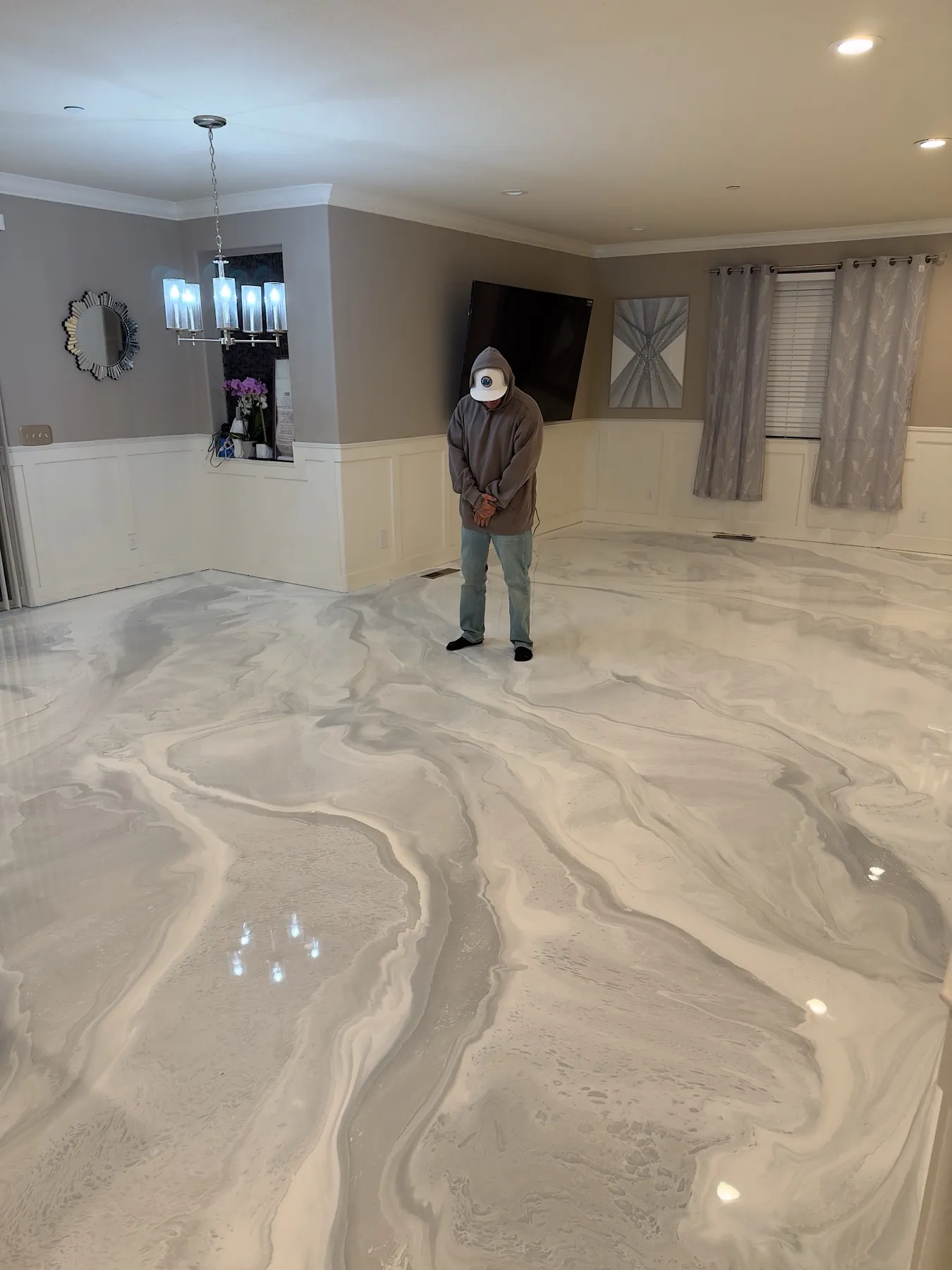 Silver and white marble metallic epoxy floor in a living room with wainscoting and a chandelier overhead